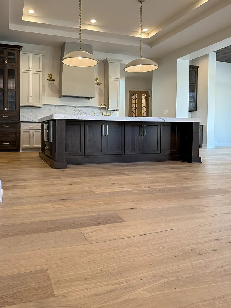 Hardwood flooring installation in San Antonio kitchen with dark island and marble countertops